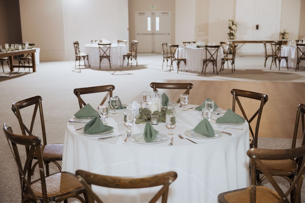 A rustic reception venue with round tables, wooden cross-back chairs, and mint green napkins set for an elegant event.
