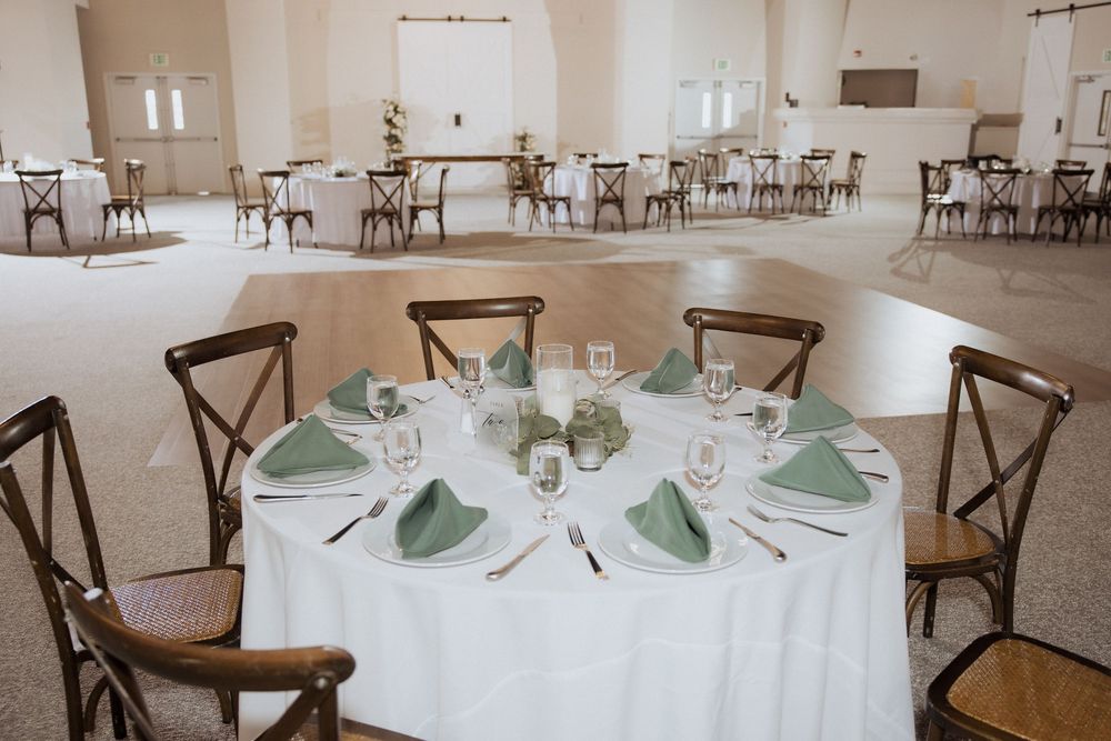 Elegant wedding reception venue with round tables set with white linens and cross-back chairs in a bright, airy space.