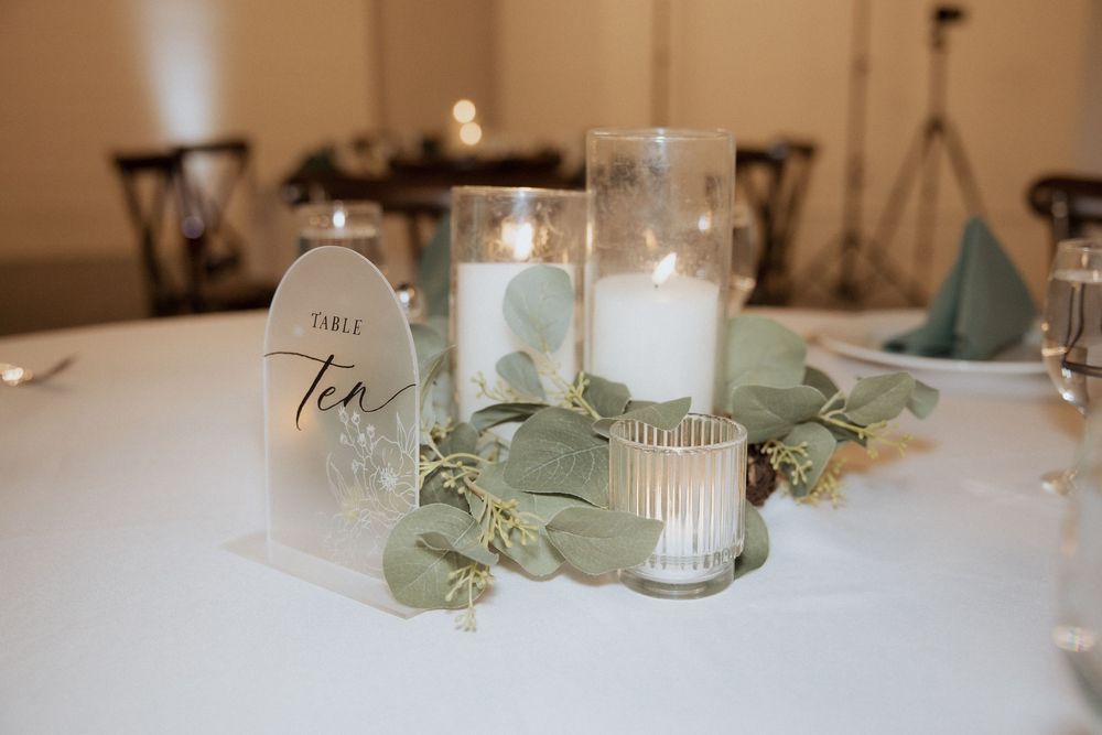 Elegant table centerpiece with frosted glass candle holders, eucalyptus leaves and white linens for wedding reception decor.