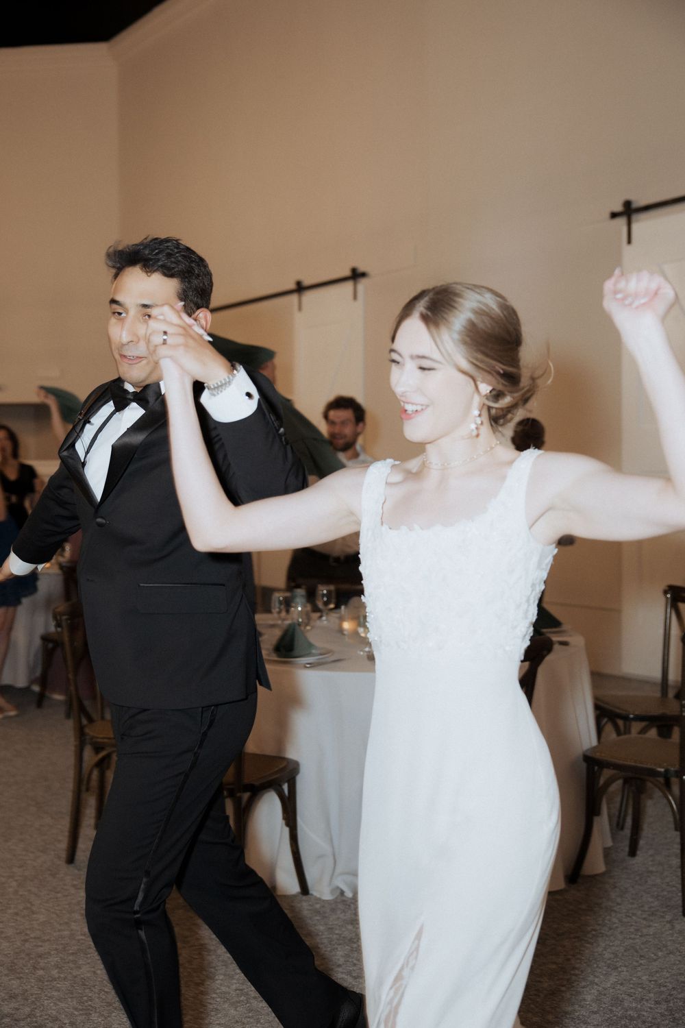 A couple in formal wedding attire dance joyfully together during their wedding reception celebration.