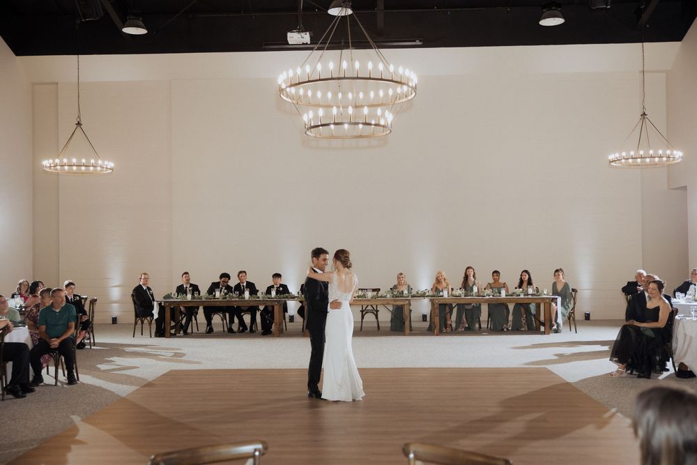 Wedding guests gather in an elegant white ballroom with crystal chandeliers during a formal ceremony.