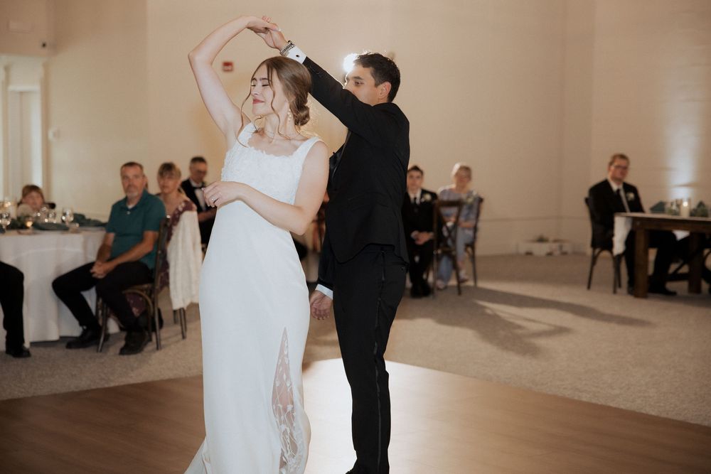 A couple shares their first dance at a wedding reception in an elegant ballroom with guests watching from tables.