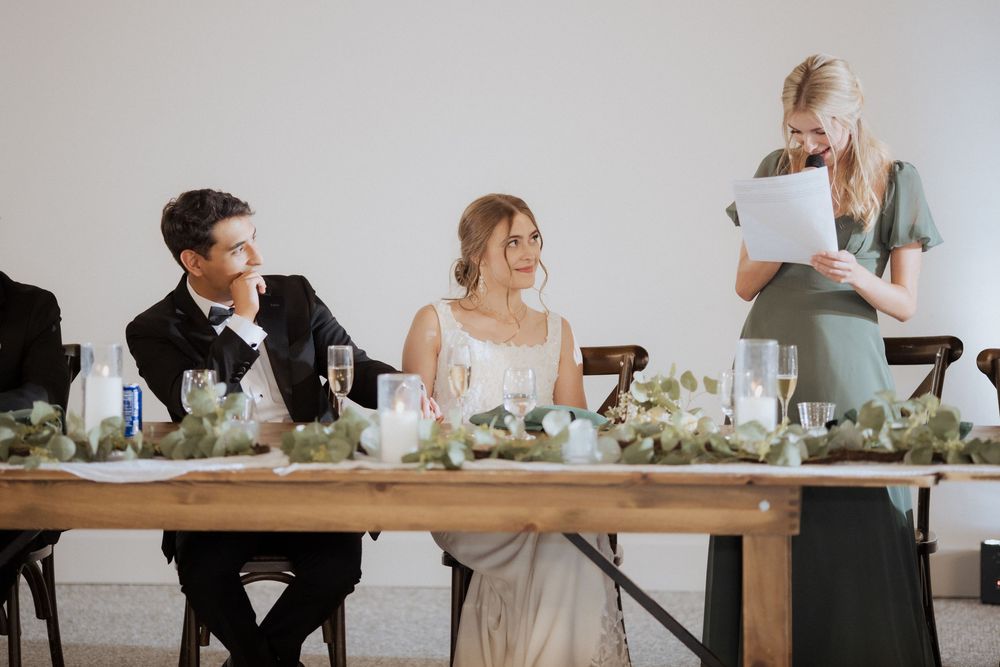 Wedding reception guests seated at long wooden tables with white floral centerpieces in an elegant dining space.