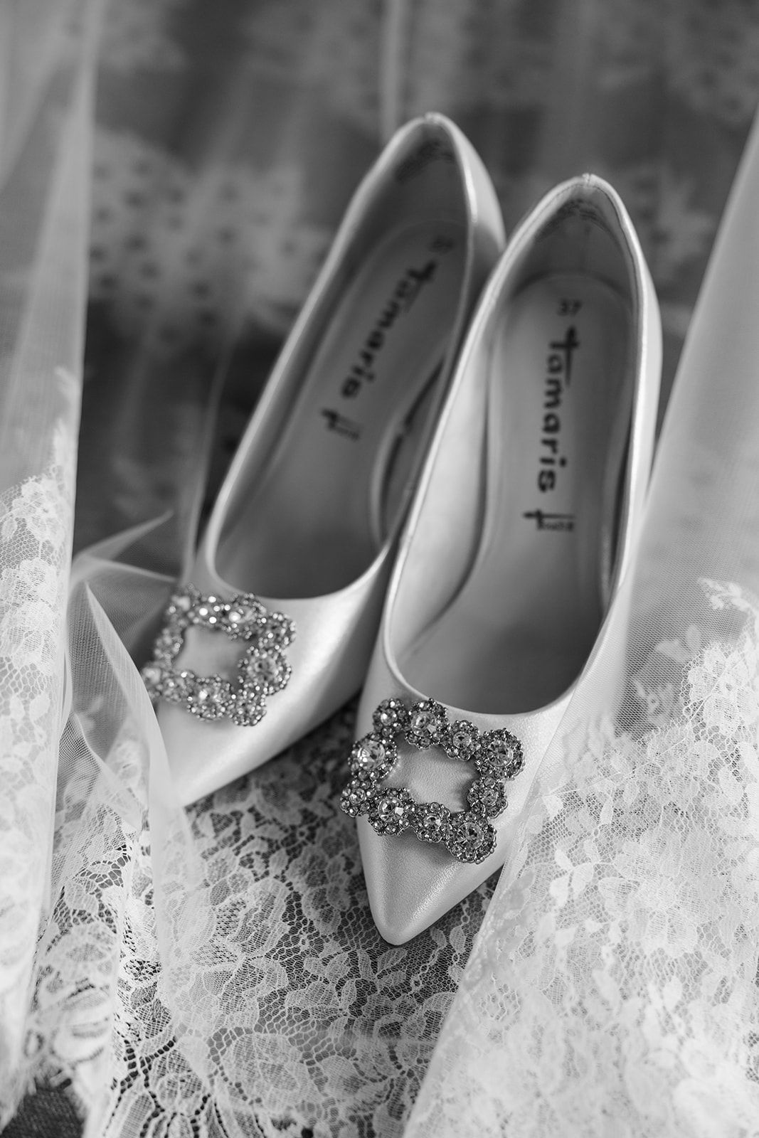 Elegant white bridal shoes with sparkling crystal embellishments arranged in a row against a lace background.