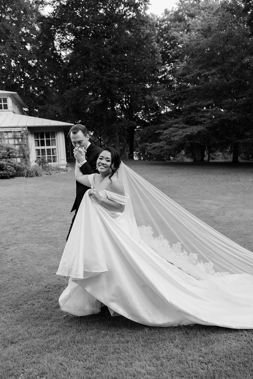 A joyful moment captured in black and white as a bride twirls in her flowing wedding gown with a long train on a grassy lawn.
