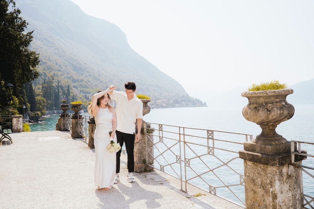 Couple enjoying scenic views from a waterfront promenade with ornate stone urns and mountains in Lake Como, Italy.