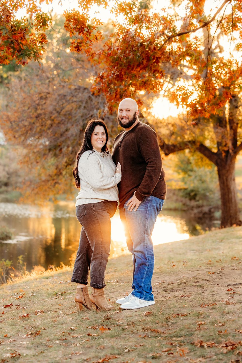 Couple poses together on an autumn hillside at sunset with golden light filtering through orange fall foliage.