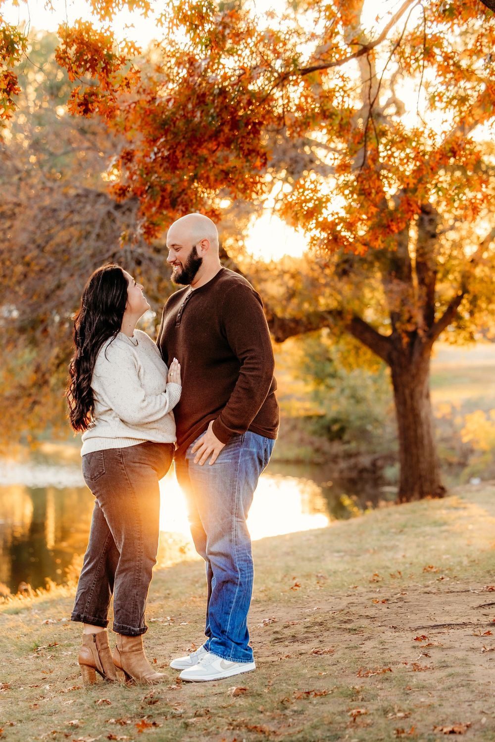 A romantic sunset engagement photoshoot in a park with autumn trees glowing in golden light.