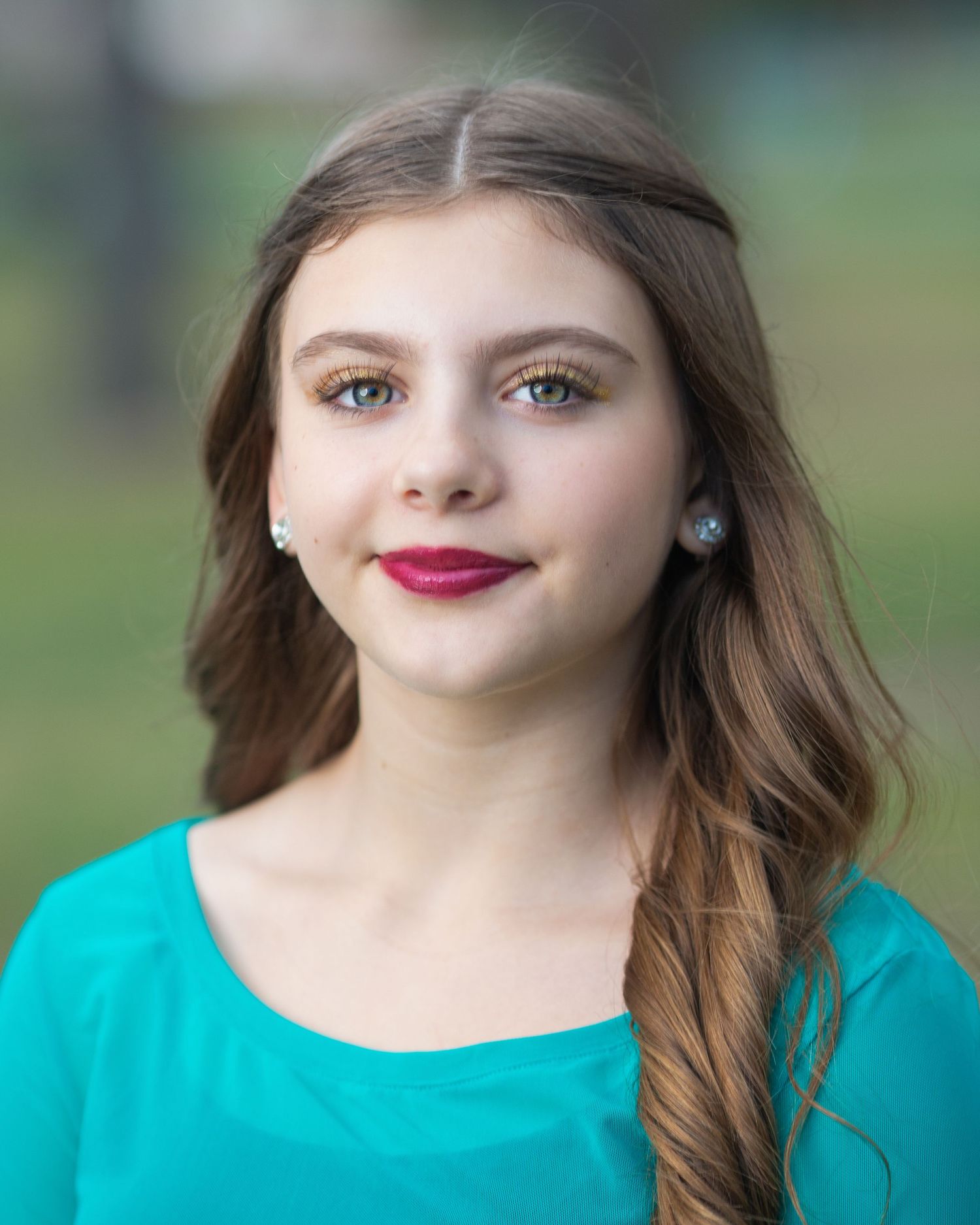 Portrait of someone in turquoise top with flowing brown hair and natural makeup.