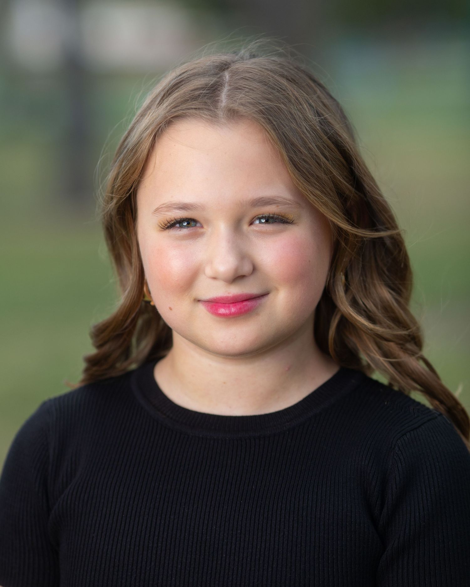Professional headshot showing wavy brown hair and black sweater against blurred background.