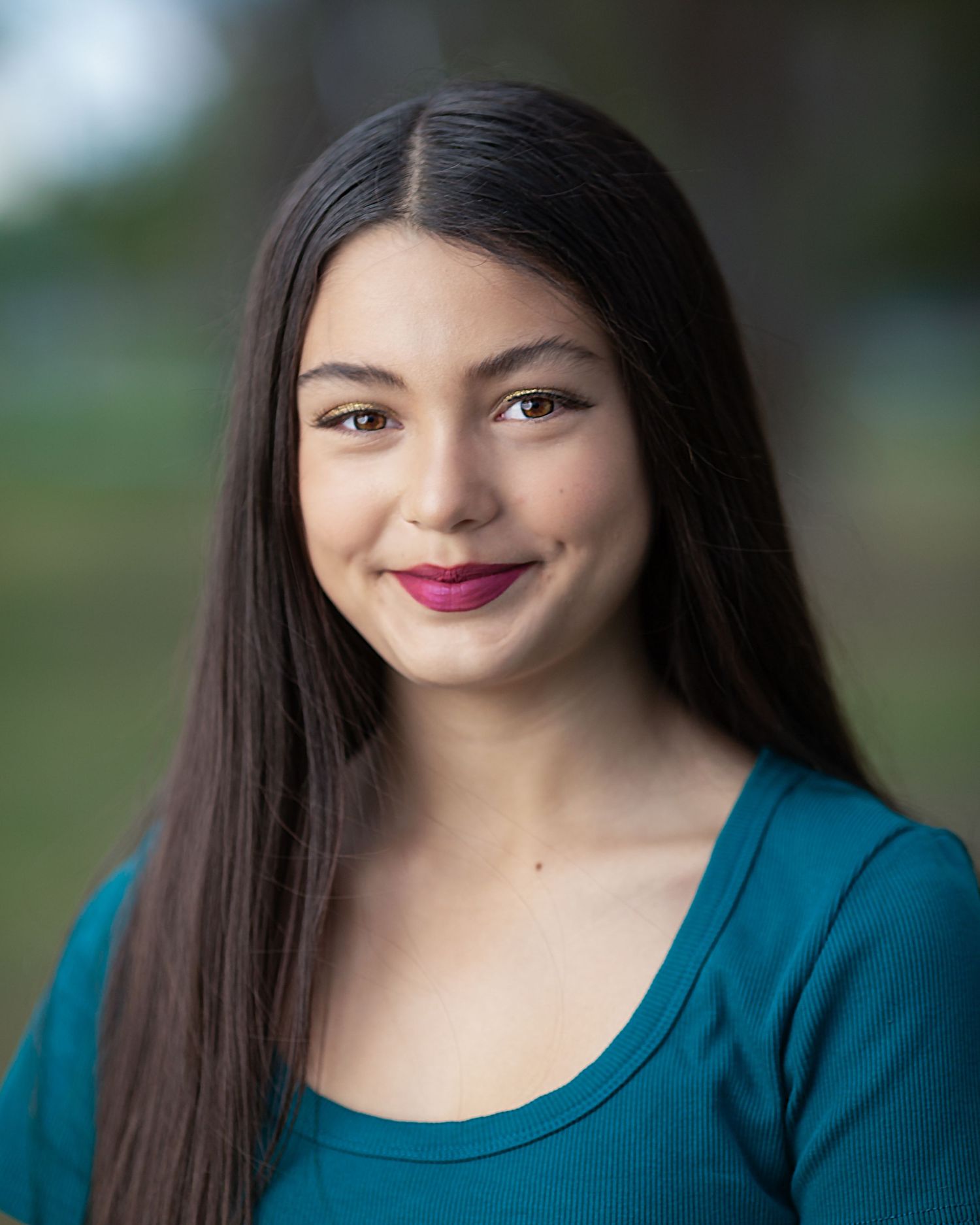 Portrait featuring long dark hair, teal top and classic makeup against soft background.