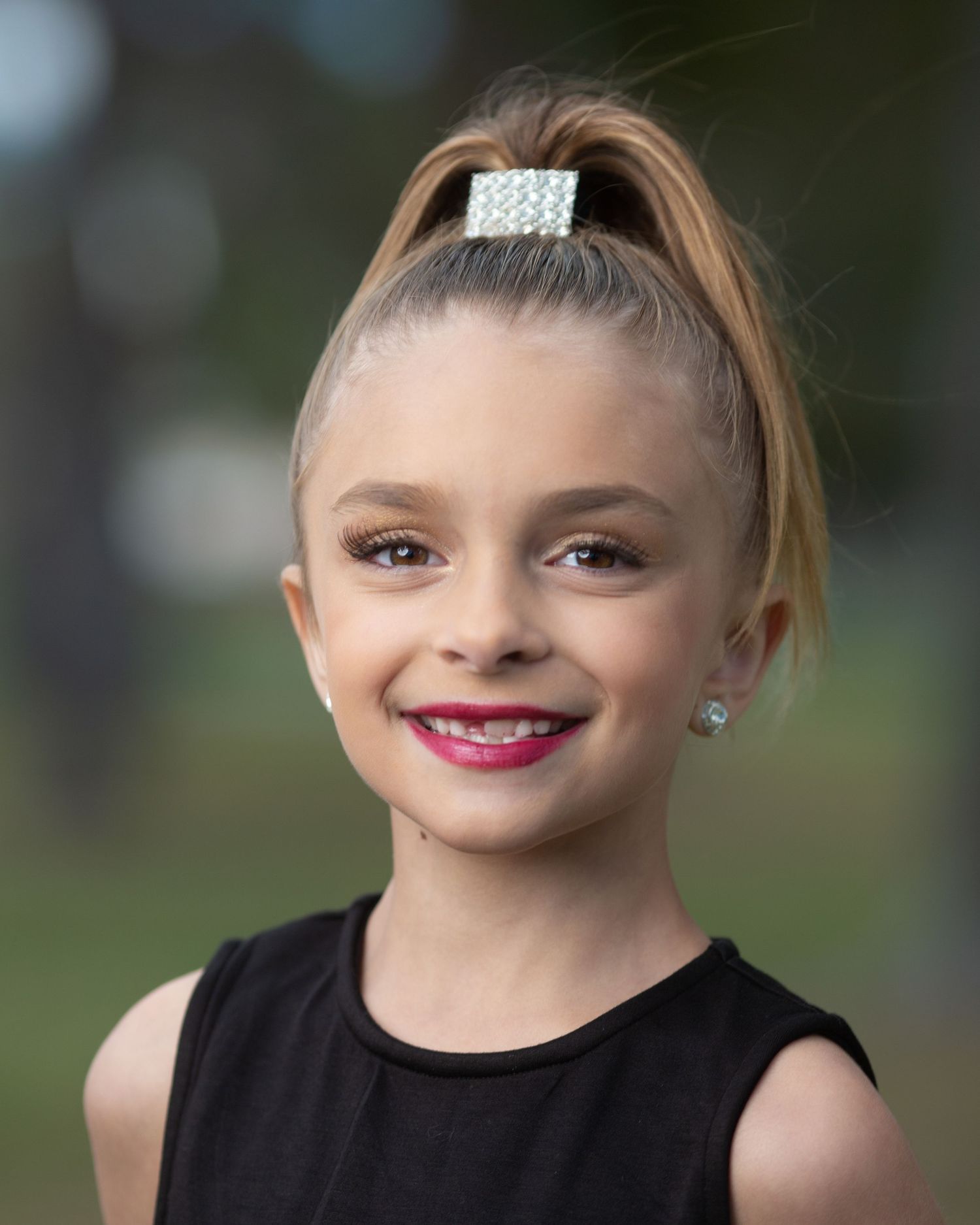Portrait with high ponytail, crystal hair clip and black sleeveless top.
