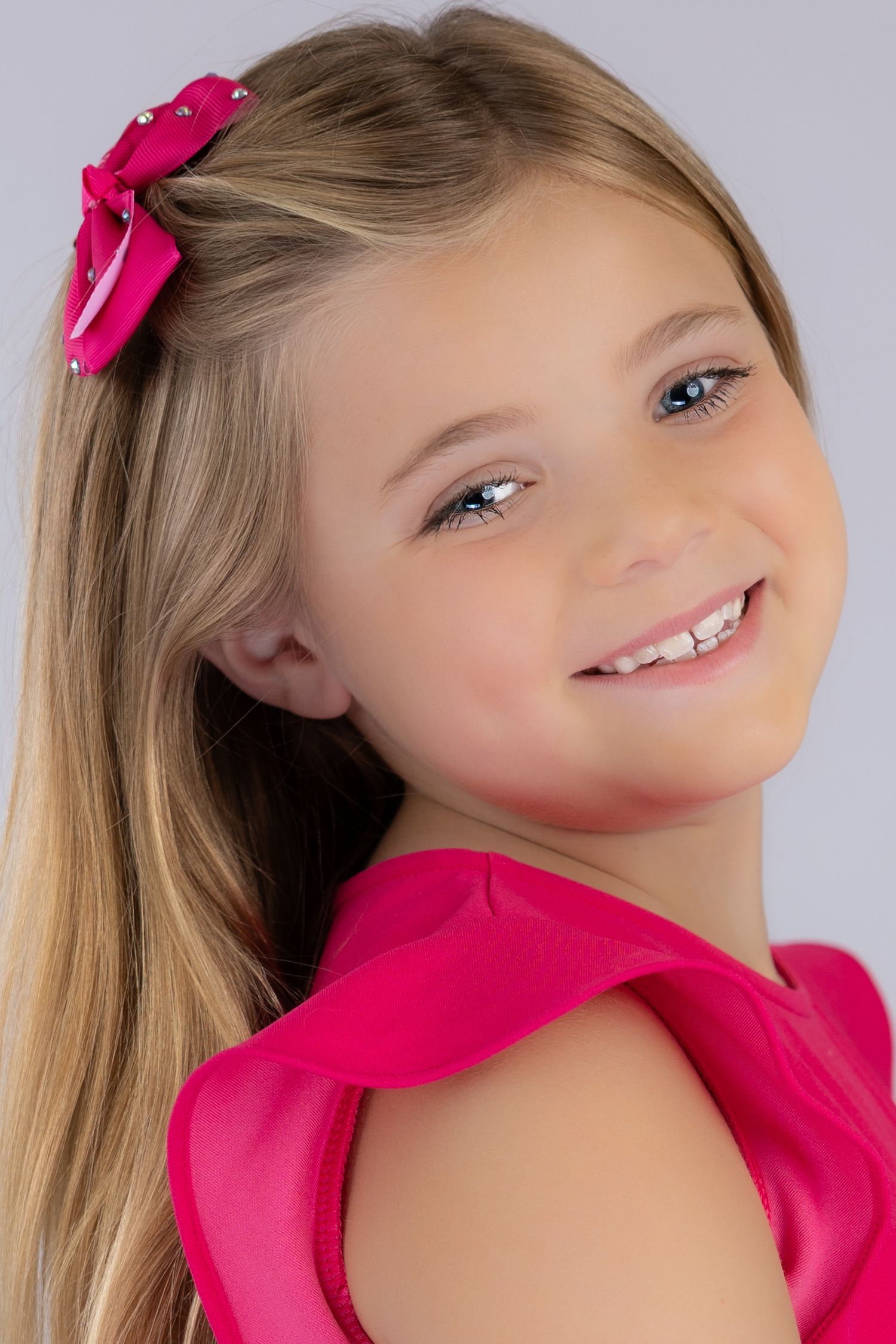 A series of four connected photos show a child with blonde hair and pink bows in a bright pink outfit against a light background.