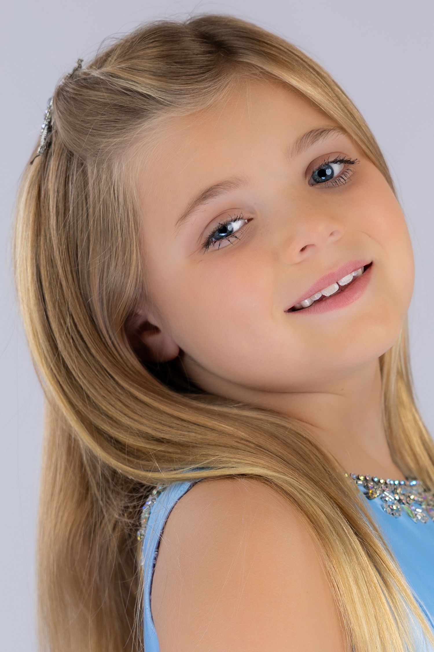 A person in a light blue top poses and smiles while looking at the camera.