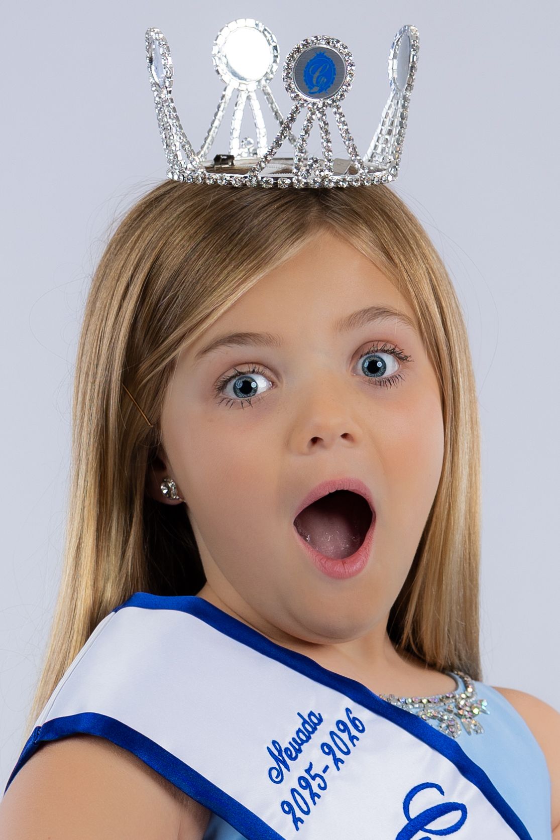 A series of four pageant style photos showing someone wearing a blue sash and crown making excited expressions.