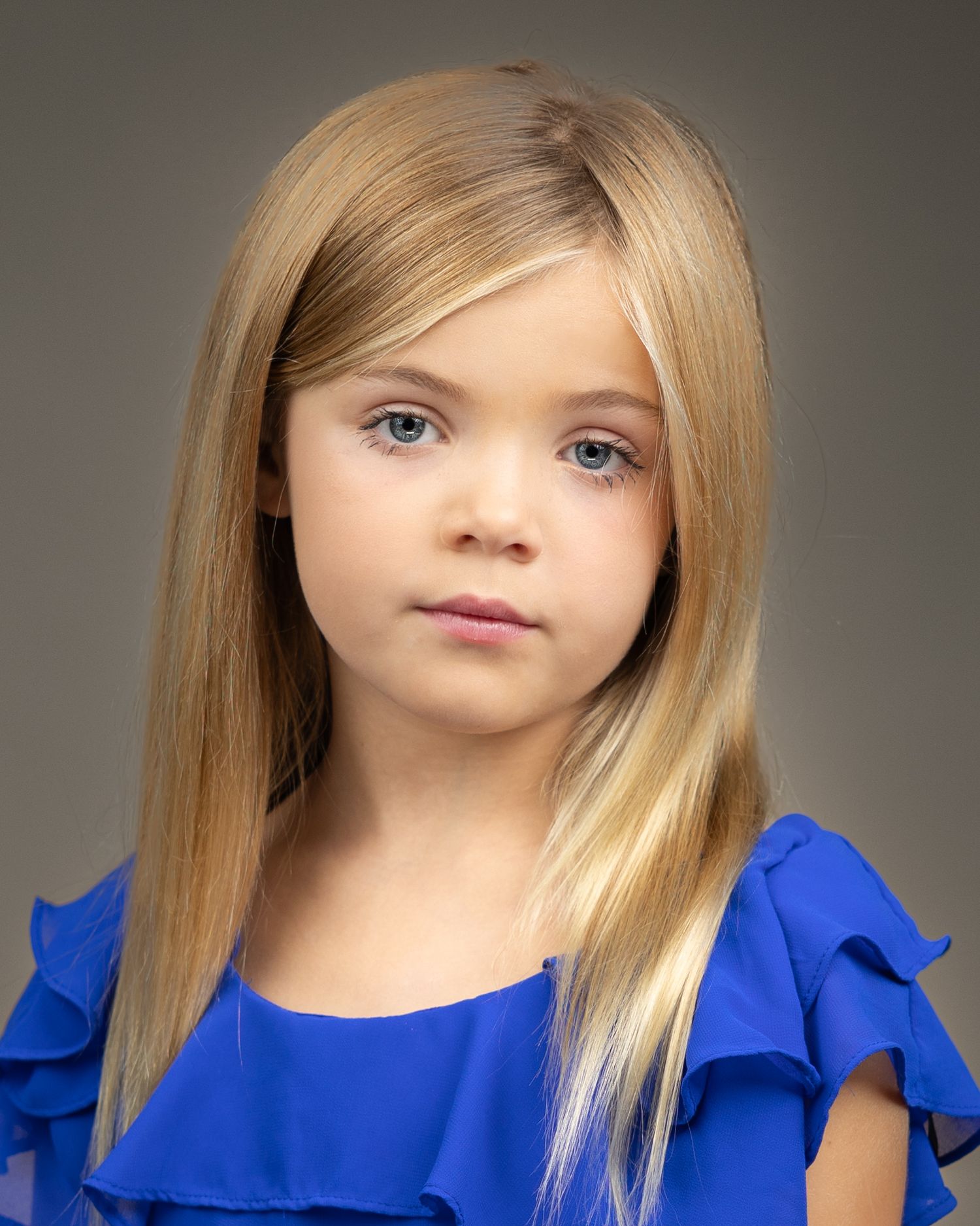 Studio portrait with royal blue ruffled sleeve top against grey background.