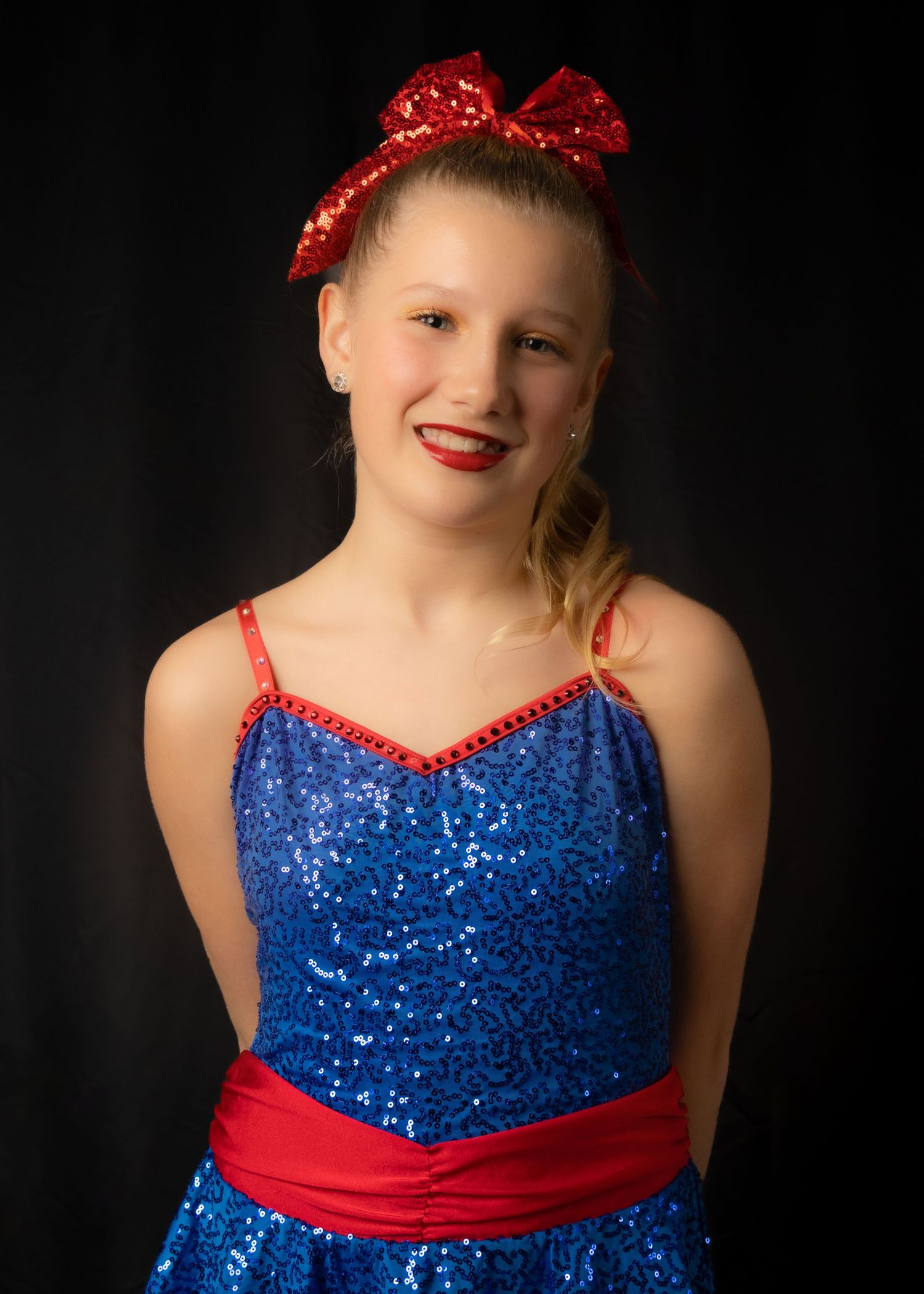 Dancer in sparkly blue and red performance costume with matching bow poses for portrait.