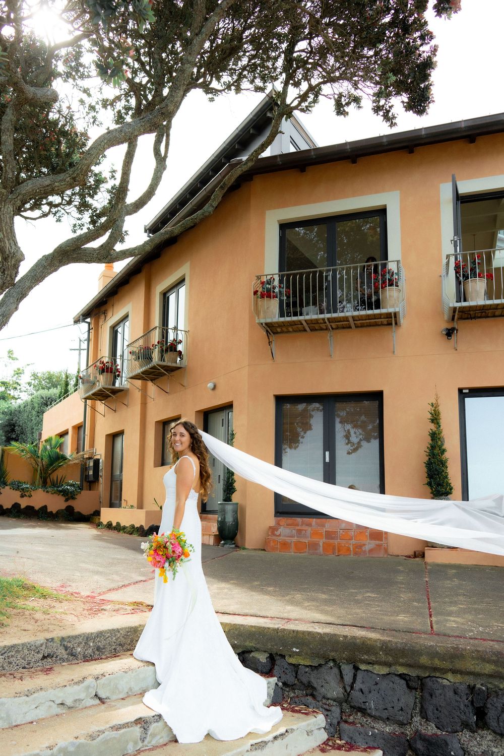 A series of photos showing a bride in a white wedding dress posing along a rustic building exterior with peach-colored walls.