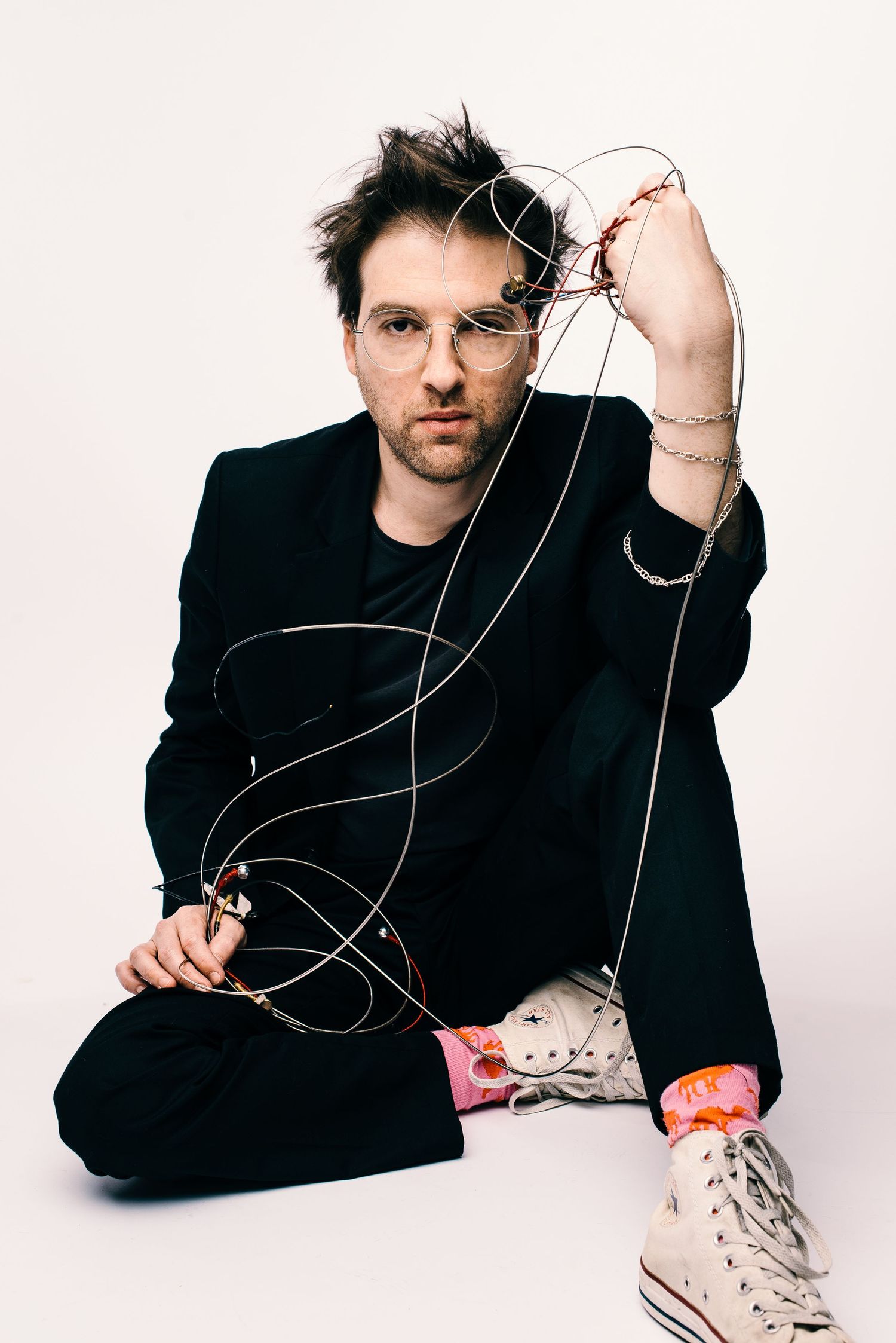 Creative portrait with tangled wires and high-top sneakers against white background.