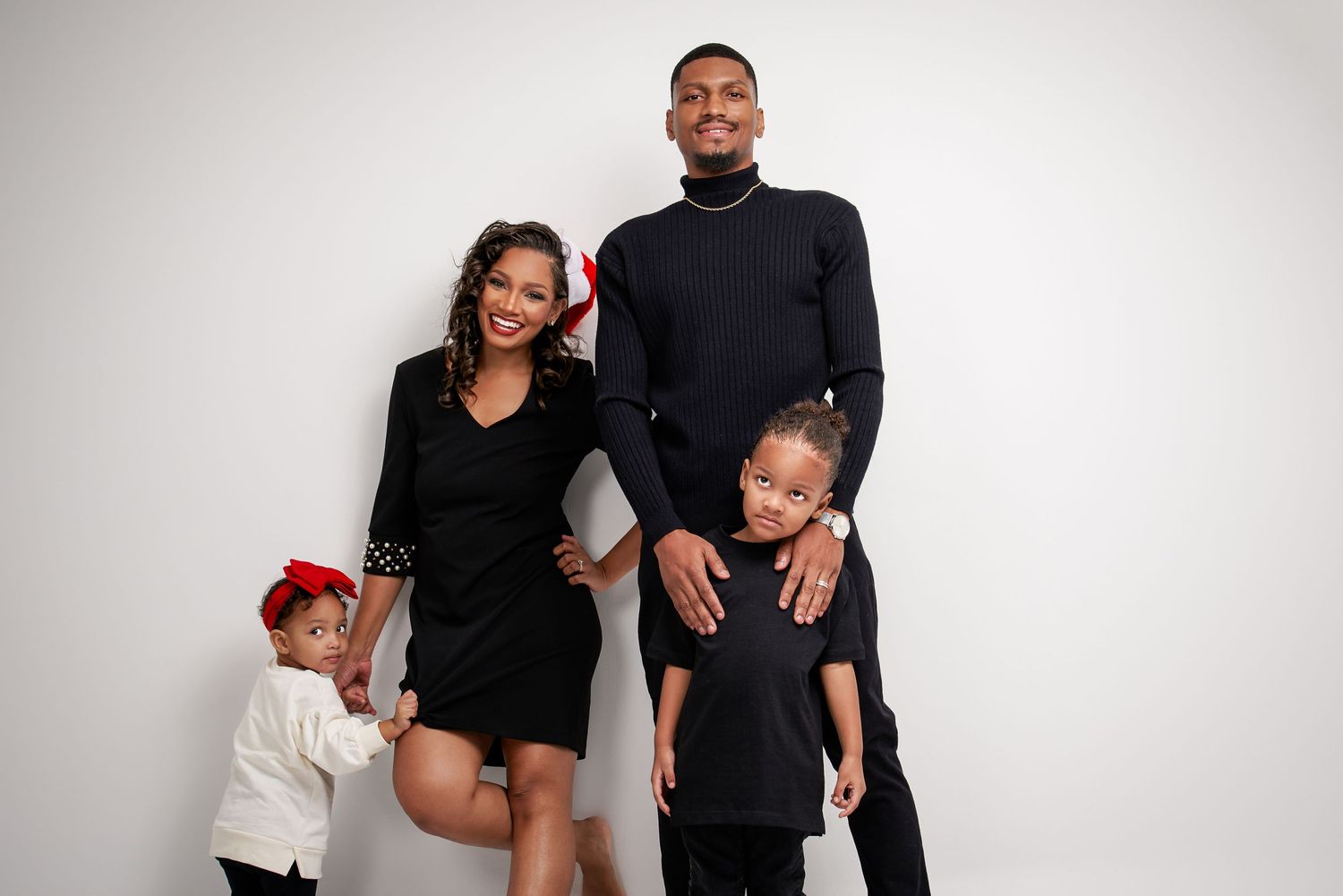Stylish family of four in black attire posing together against white studio background.