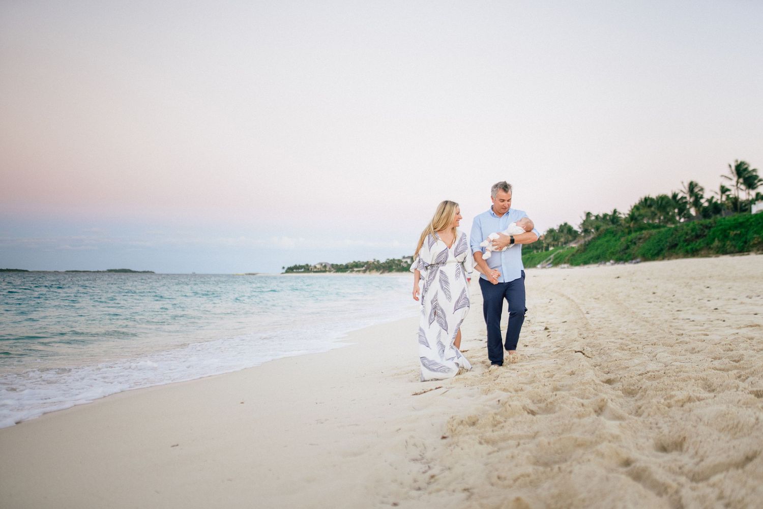 Couple walking along beach shore during sunset in casual white attire.