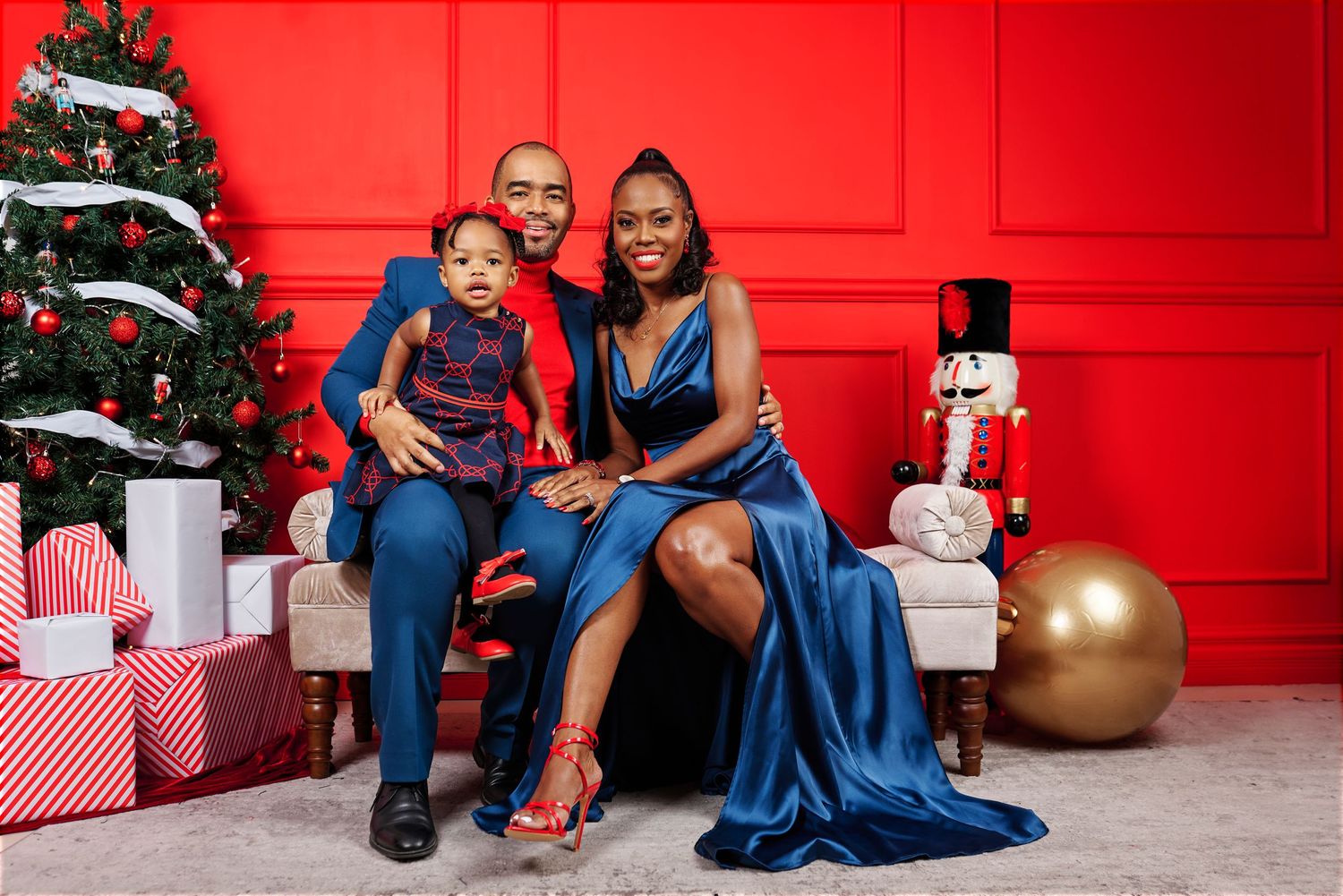 Holiday family portrait with Christmas tree and decorations against bright red wall.