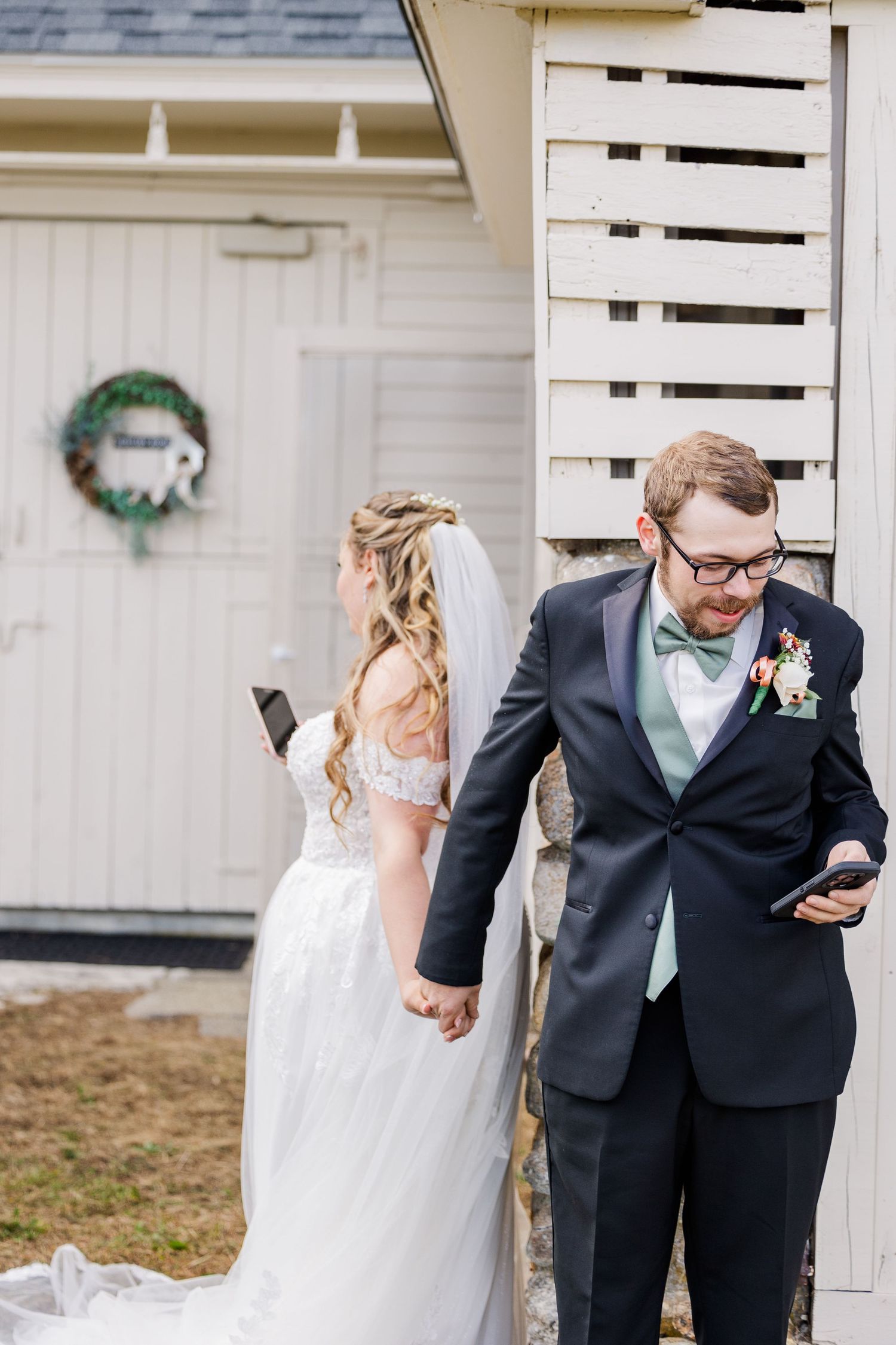 A couple in wedding attire looks at their phones during a first look moment.
