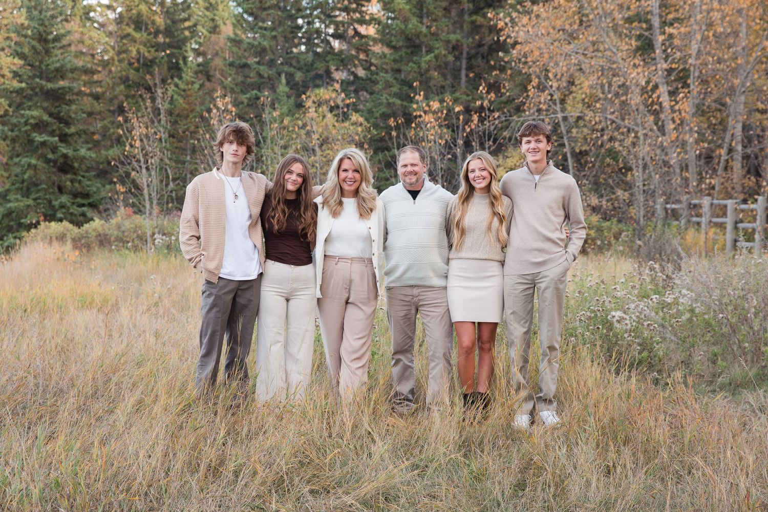 Family group portrait in coordinated neutral outfits standing in mountain meadow at sunset.