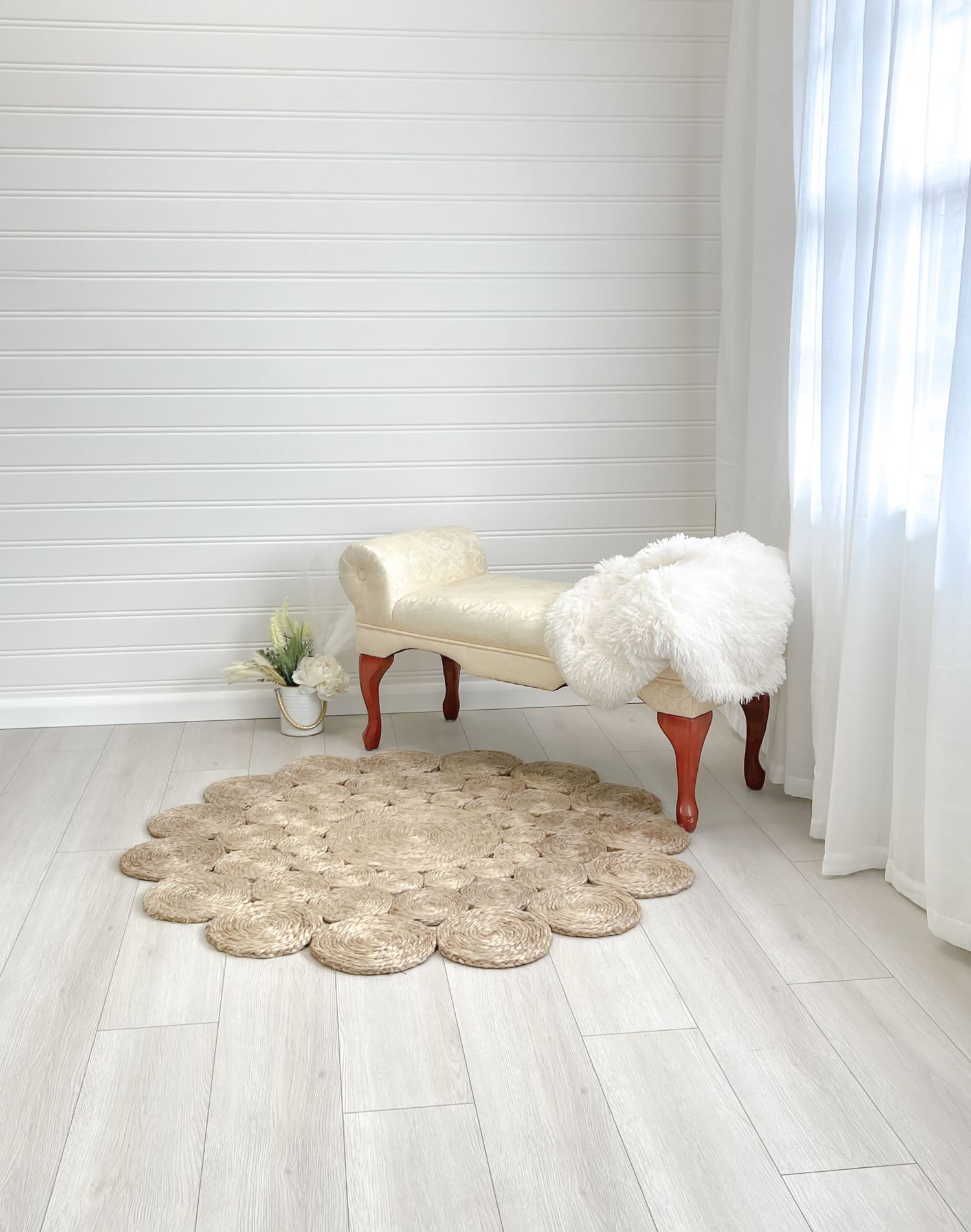 A white plush rug on light wood flooring next to sheer curtains in a bright room.