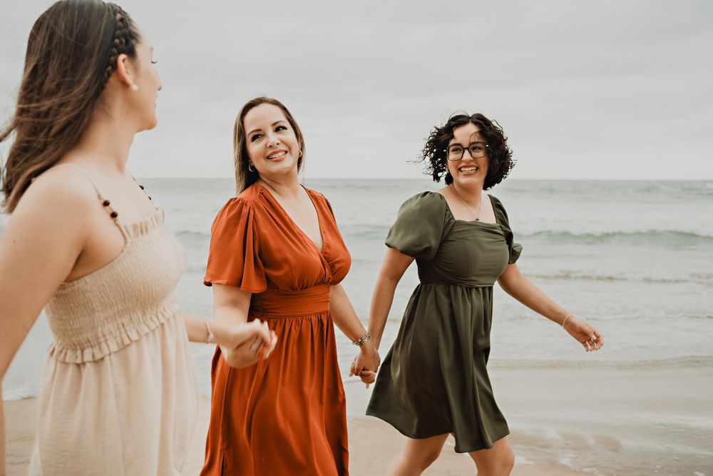 Mother and daughter smiling at the other daughter, holding hands by the ocean