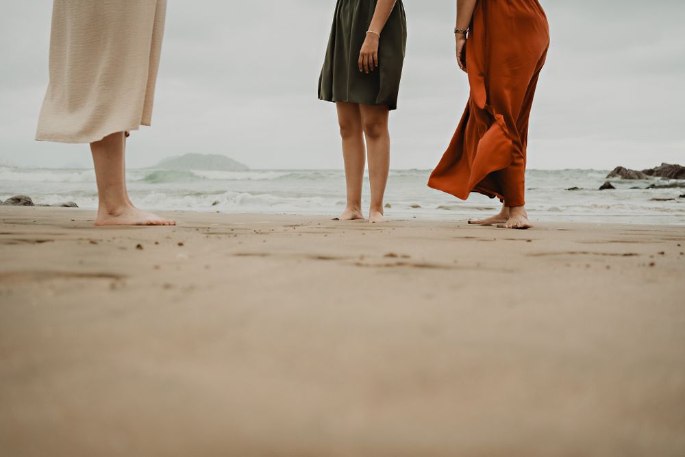 Artistic shot of the beach, showing the legs of mother and daughters, dresses blown by the wind
