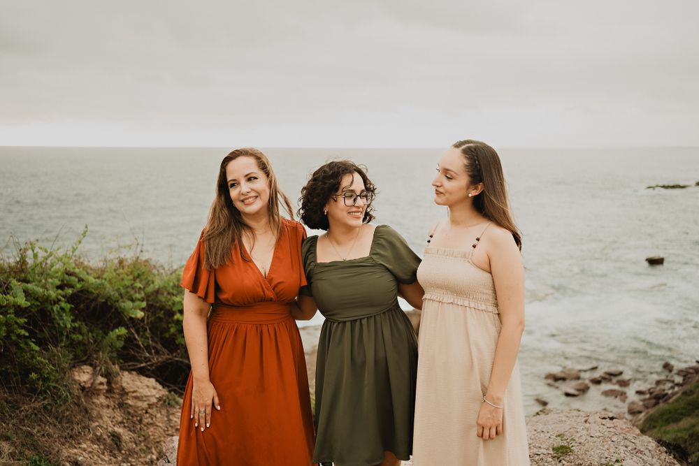 Mother and daughters happily standing on a cliff, ocean backdrop, cloudy sky