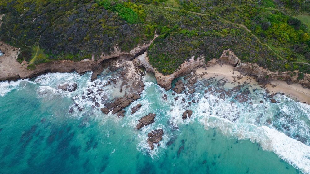 Aerial view of turquoise ocean waves crashing against rocky coastline with sandy beaches.