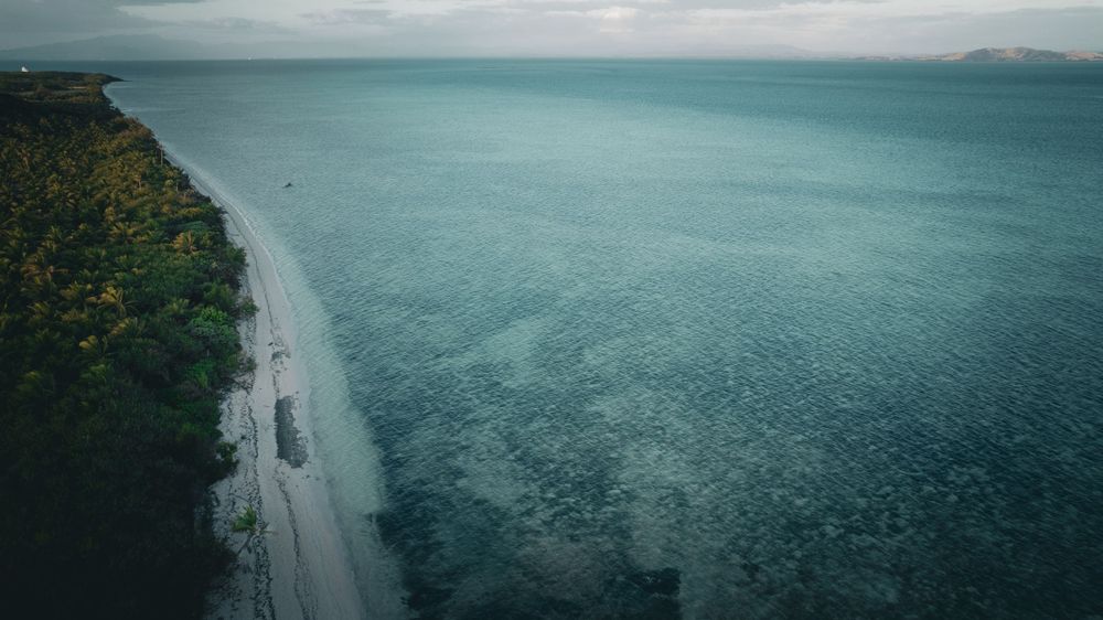 Aerial view of coastal road winding along turquoise ocean waters and green cliffs.