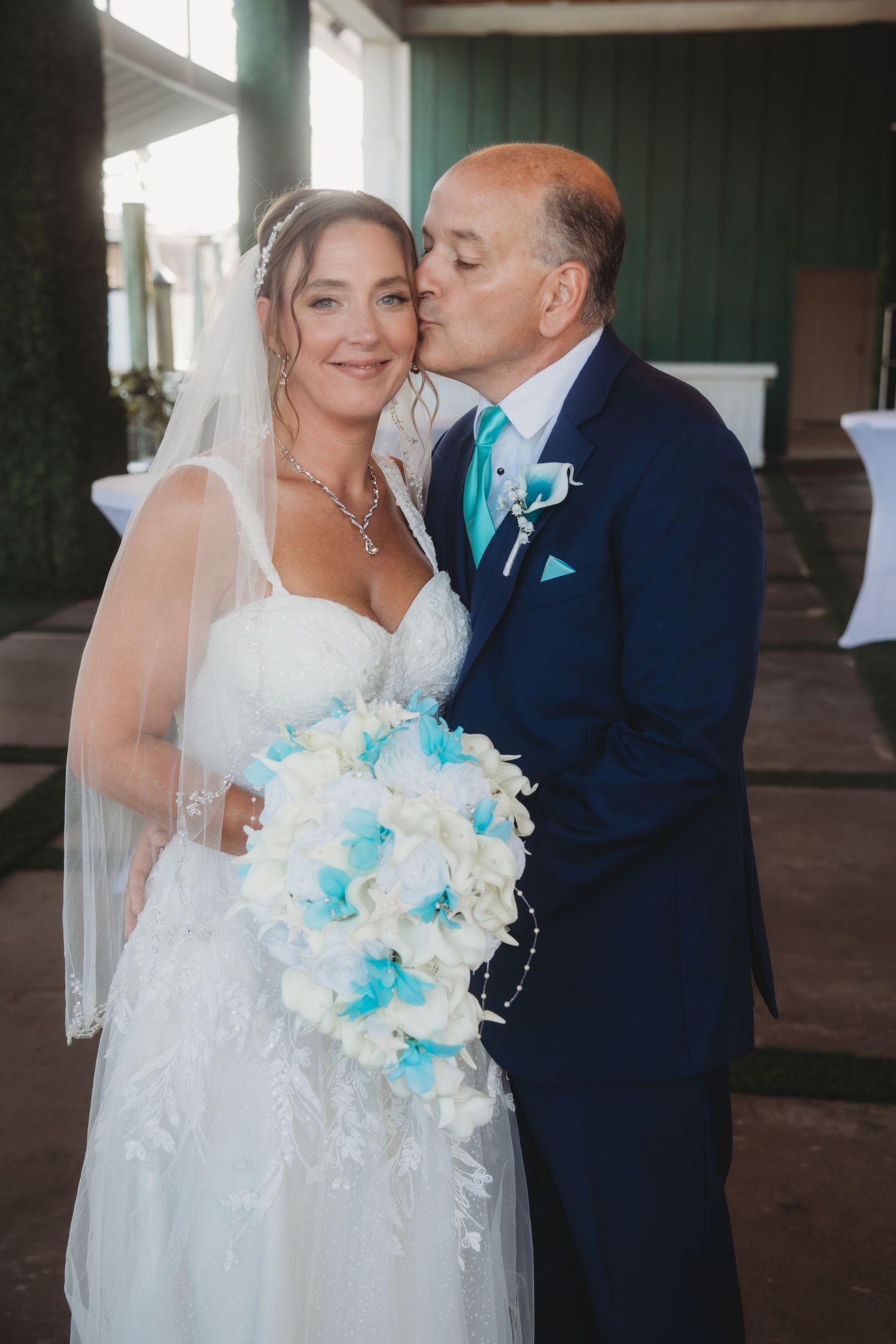 Tender wedding moment captured between couple with bride holding blue and white bouquet.