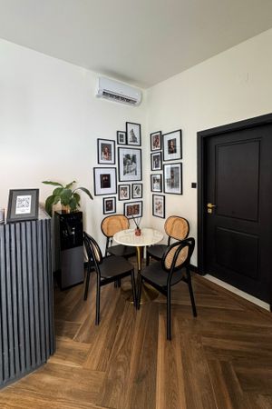 A corner dining nook with black and rattan chairs, round table, herringbone wood floors and gallery wall of framed photos.
