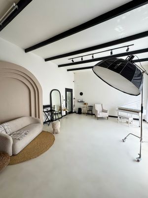 Modern photography studio interior with white walls, exposed beams, arched nook, and professional lighting equipment.