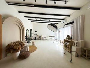 Modern white photography studio interior with arched wall, exposed beams, and professional lighting equipment.