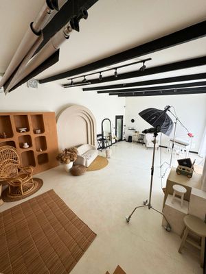 Professional photography studio interior with lighting equipment, rattan chair, built-in shelving and white walls.