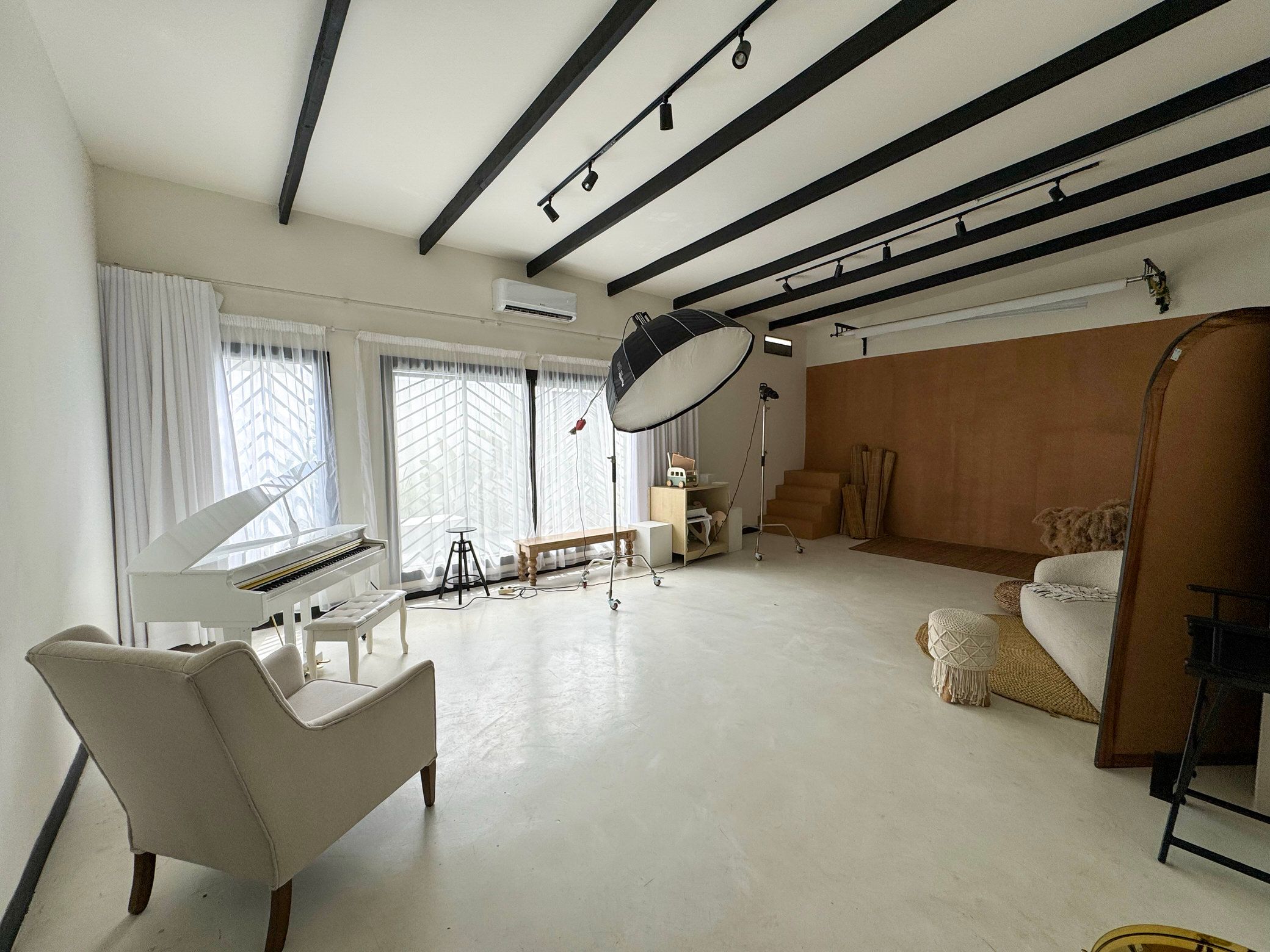 Modern studio space with exposed beams, white chairs, hardwood accent wall and large bay windows streaming natural light.