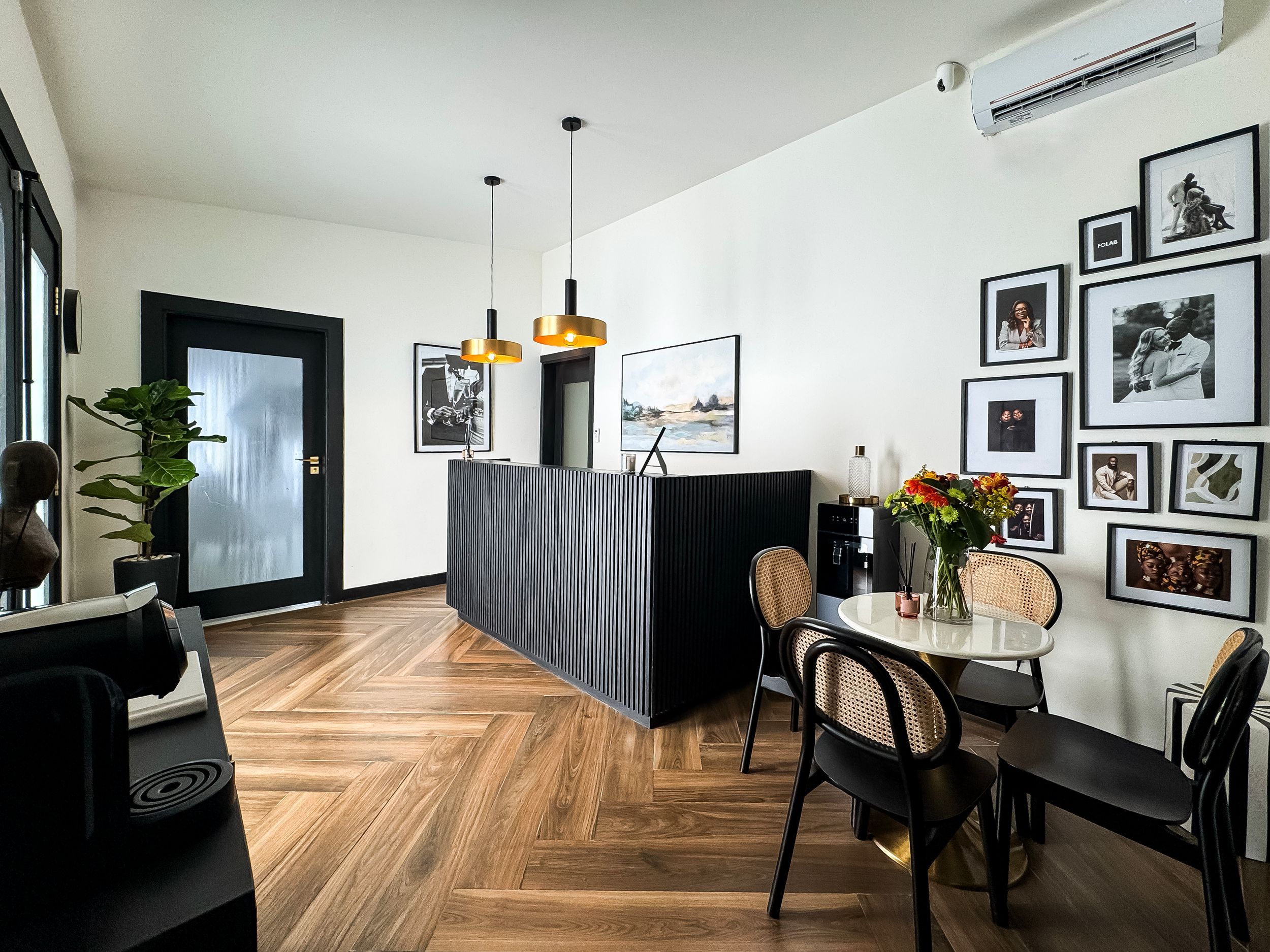Modern dining area with herringbone wood floors, black and white gallery wall, and pendant lighting above a dark partition.