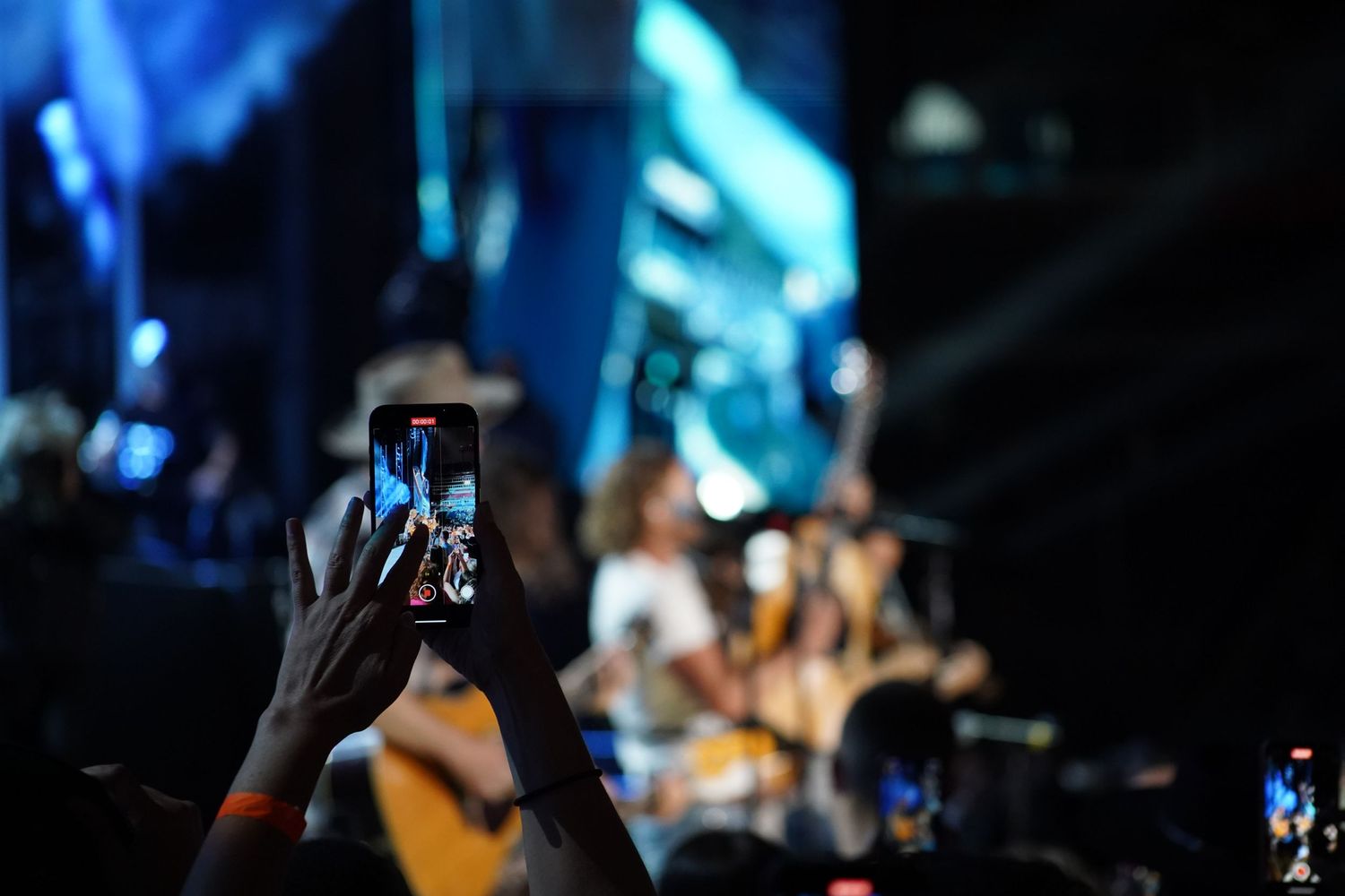 Concert crowd holding up phones to capture performance in blue lighting.