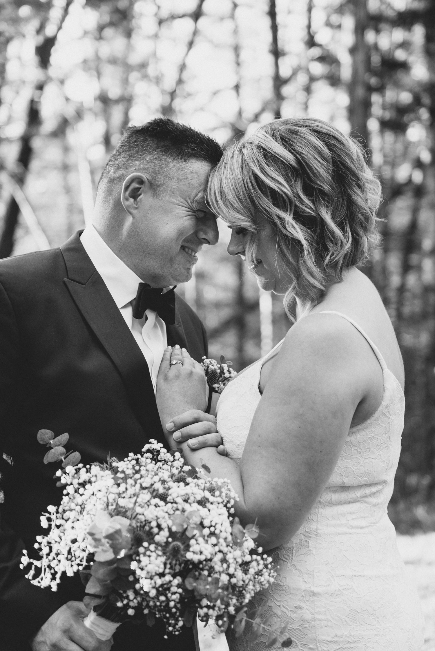 A romantic black and white wedding moment captured on a wooden deck surrounded by trees.