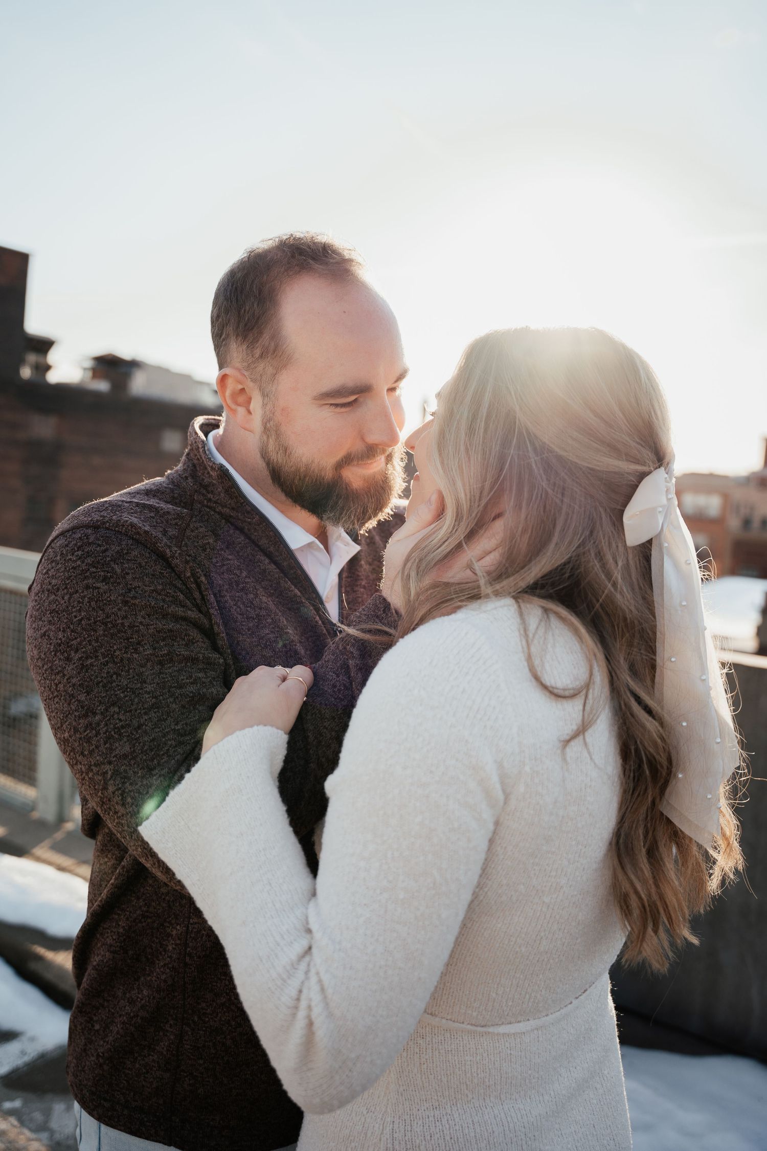 A romantic winter couple embraces outdoors during sunset with soft lighting and warm sweaters.
