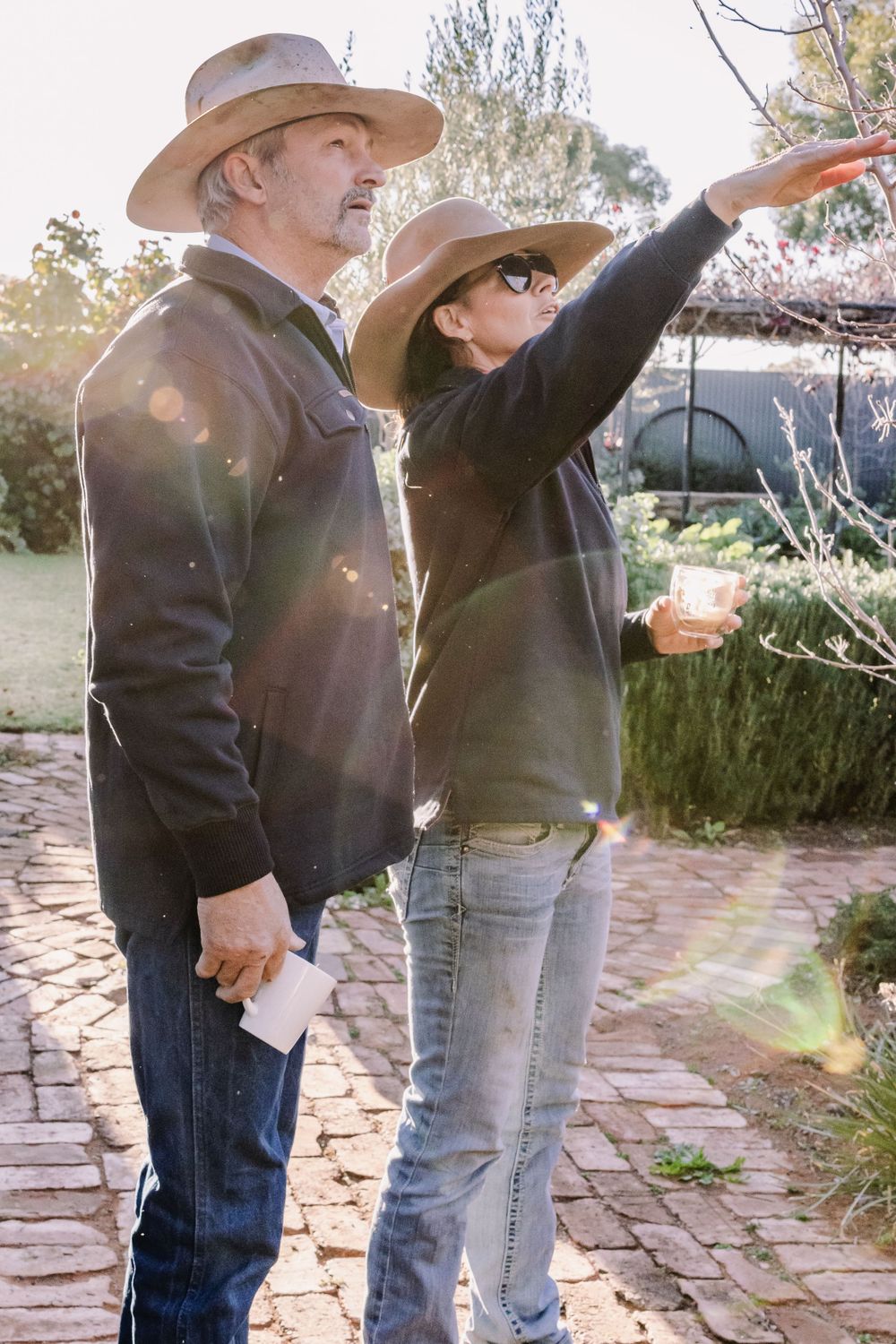 Two people in cowboy hats explore outdoor garden path while pointing at something in distance.