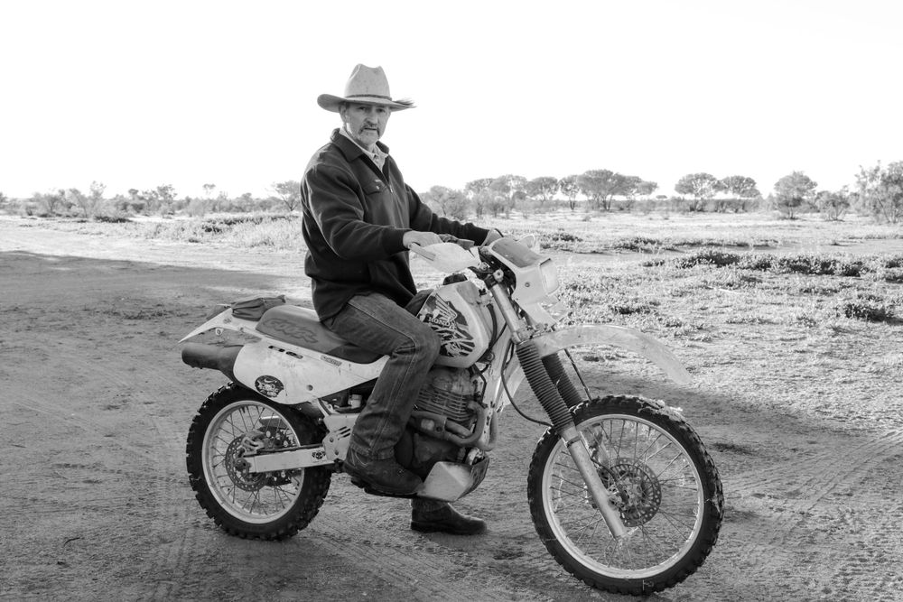 Black and white photo of person on dirt bike in desert setting.