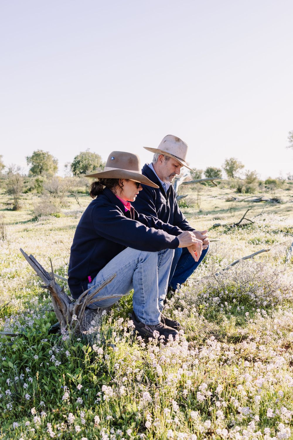 Two people in cowboy hats sit in a field with wildflowers during a peaceful outdoor moment.