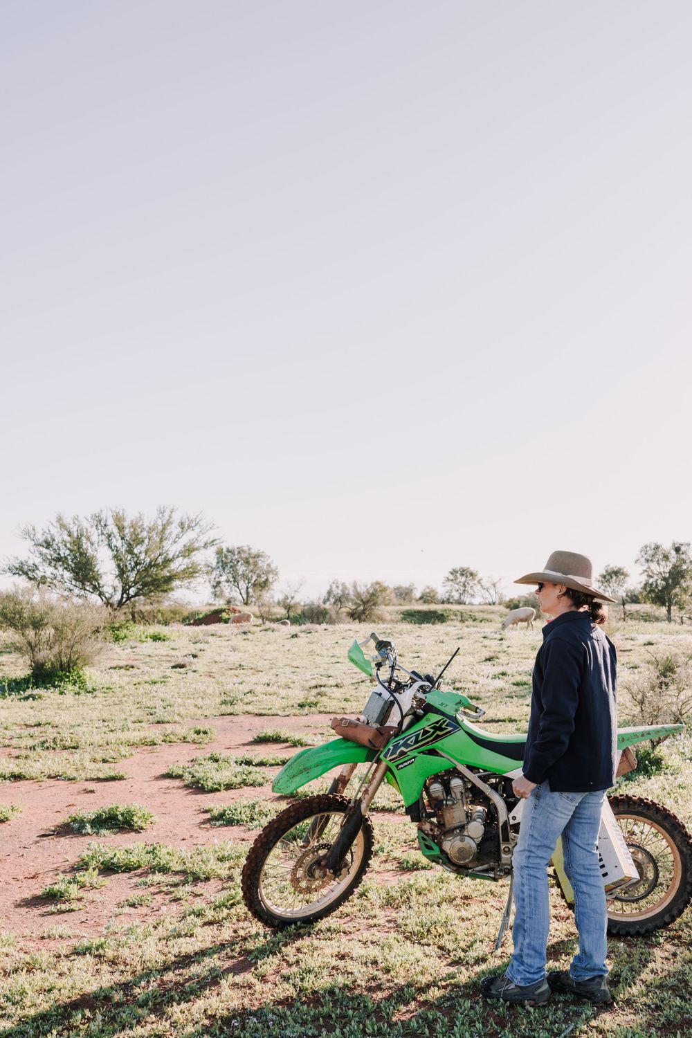 Green dirt bike parked in arid desert landscape with scattered vegetation.