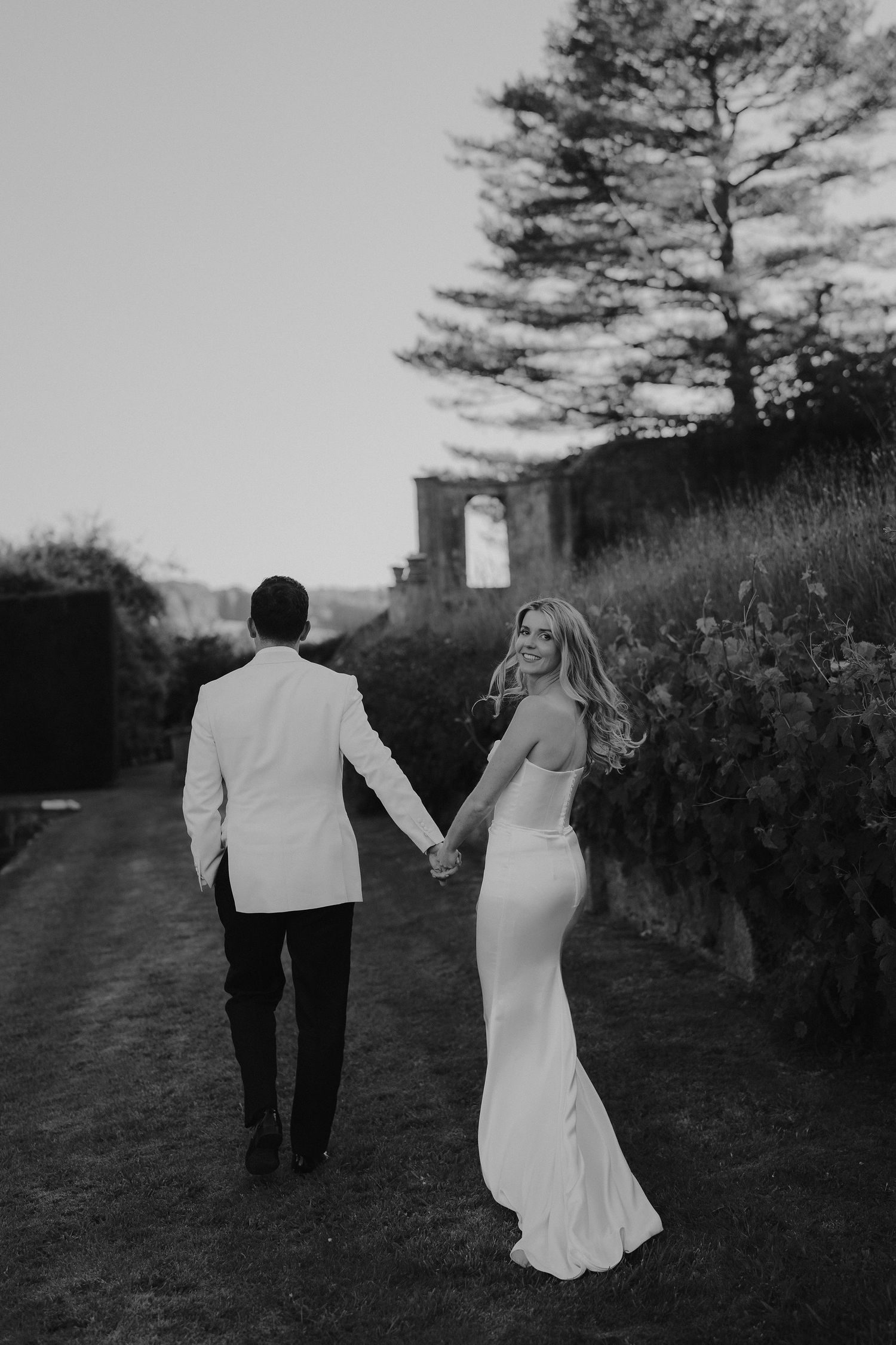 bride smiling over her shoulder while groom leads her away at hamswell house wedding in bath