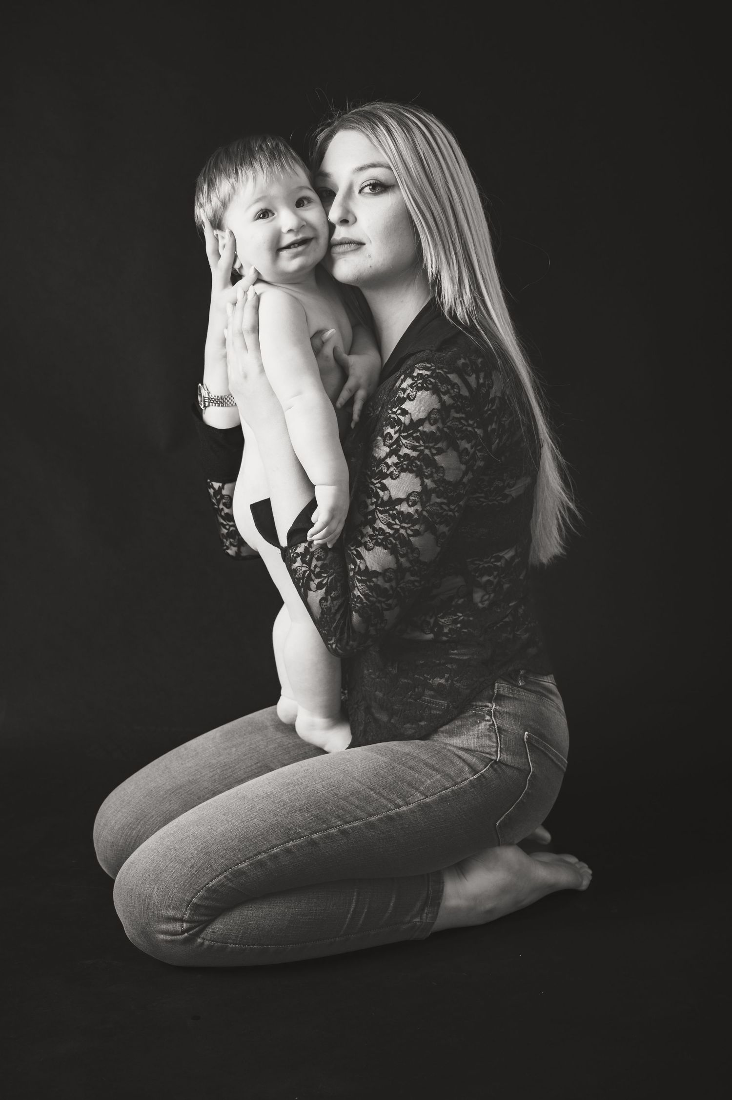 Artistic black and white studio portrait of parent and child against dark background.
